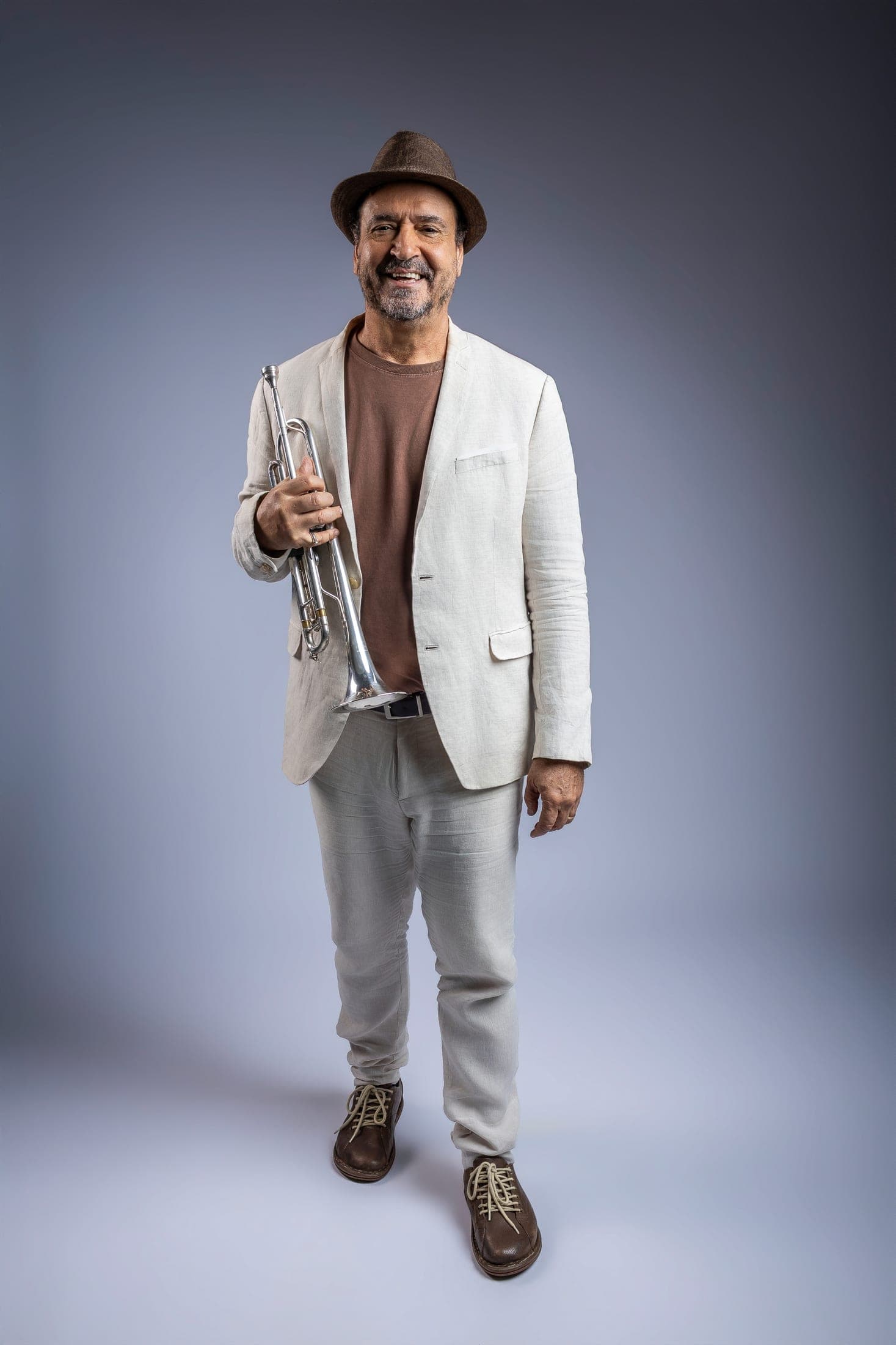 Silvério Pontes de corpo inteiro, de terno de linho claro e chapéu, sorrindo com o trompete na mão