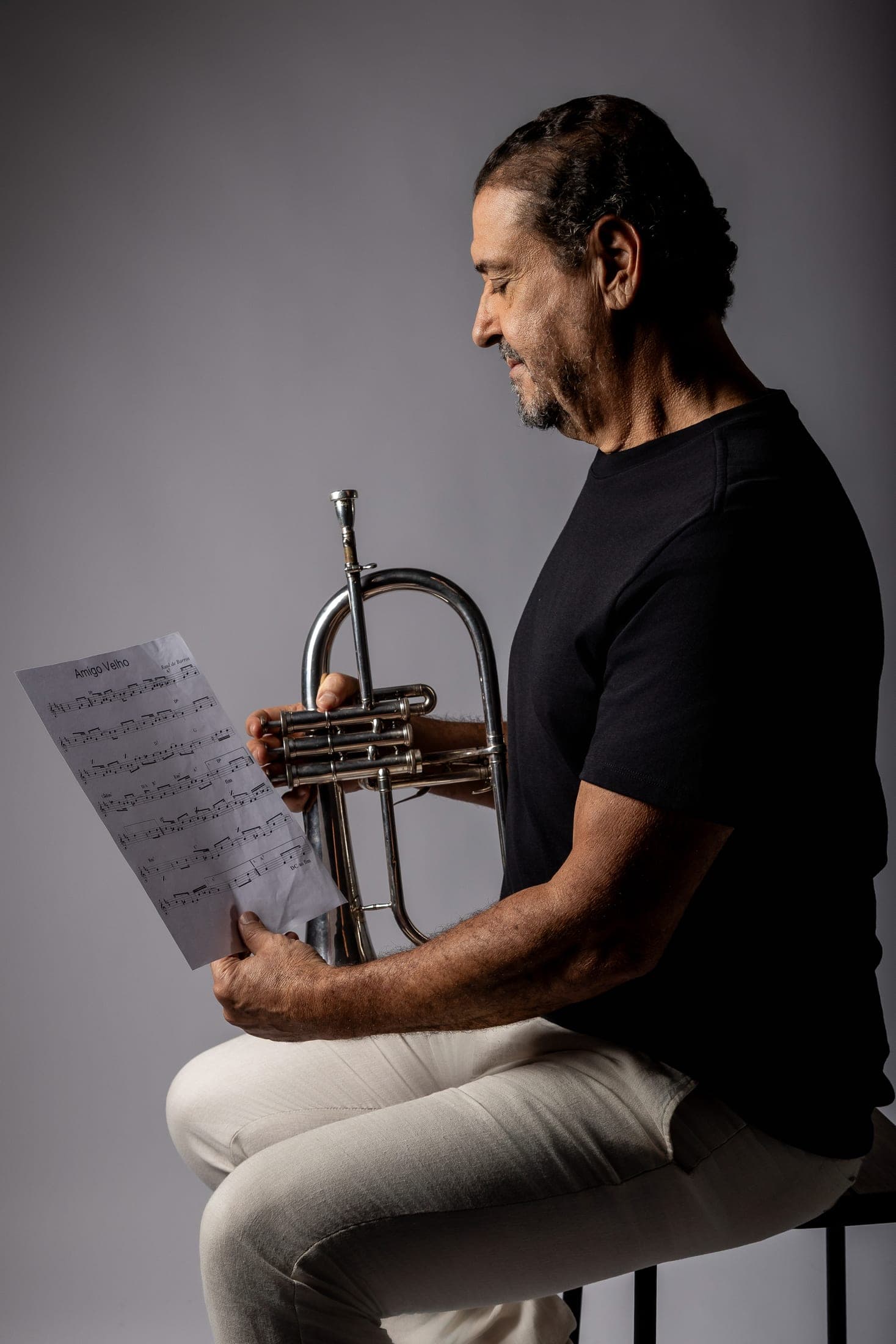 Silvério Pontes sentado, lendo partitura com o flugelhorn no colo